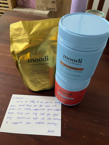 Customer's Moodi Strawberry Watermelon product on a wooden table with a gifted Mug Cake and a handwritten thank you note.