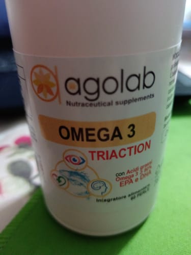 Primo piano del flacone bianco dell'integratore Omega 3 del recensore su una superficie verde.