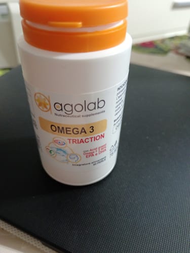 Cliente mostra il flacone di integratori Omega 3 Triaction di agolab su una superficie scura.