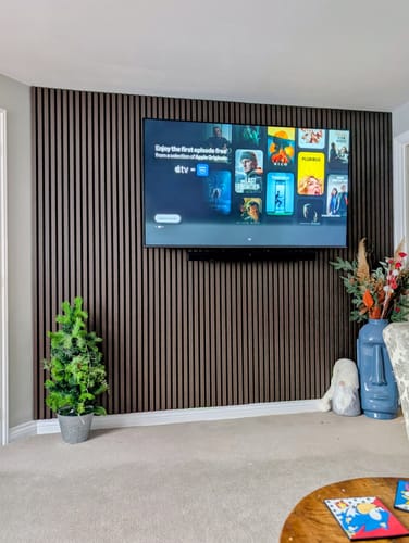 Reviewer's living room with smoked oak acoustic slatted wall panels installed as a modern feature wall behind a TV.