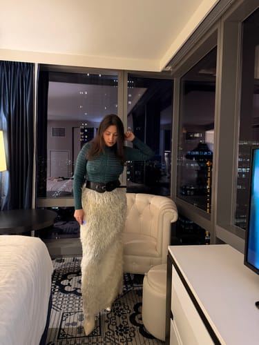 Customer wearing the green Naked Print Mock Neck Top with a long skirt and wide belt in a hotel room.