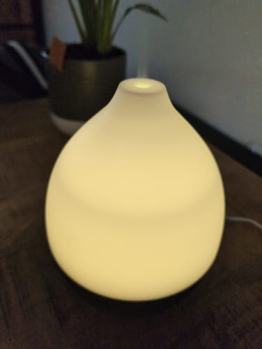 Recensent toont de Nimbus 2.0 diffuser verlicht als een warmgeel nachtlampje terwijl het nevel verspreidt.