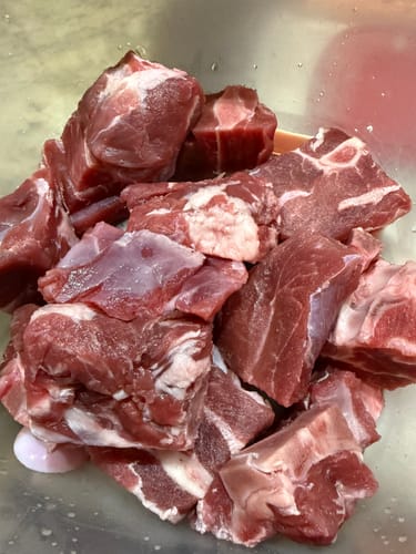 Customer's raw Halal Goat Cubes-Gosht piled in a container before cooking.