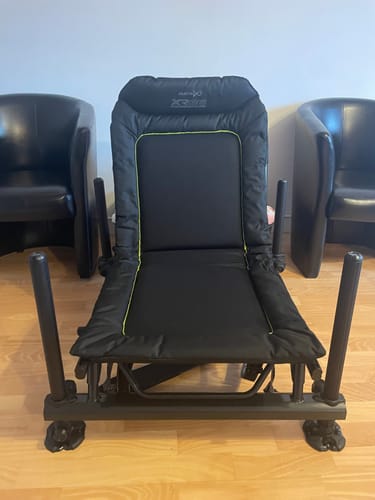 Klant toont de gewatteerde zwarte XR36 PRO ACCESSORY CHAIR, opgesteld op een houten vloer.