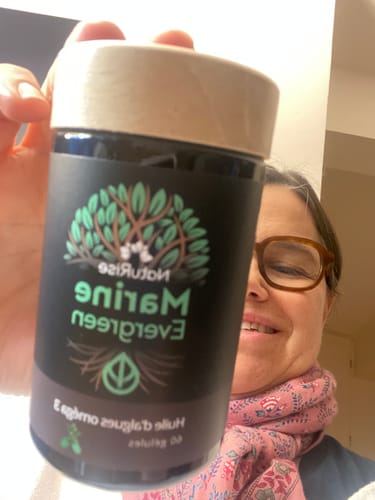 Une cliente sourit en tenant son flacon d'Huile d'algues oméga 3.