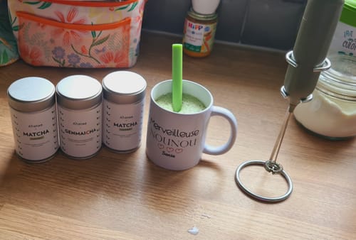 Photo d'une cliente montrant ses boîtes de thé Matcha, une tasse de poudre de matcha et un mousseur sur un comptoir.