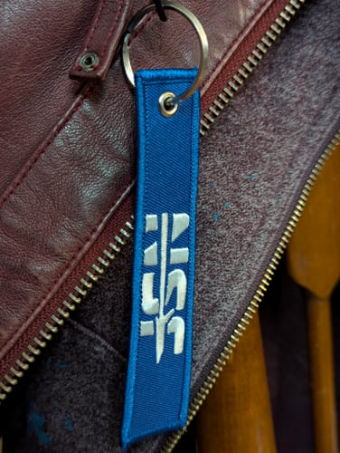 Close-up of a customer's blue NSF Keyflag with the white embroidered logo, attached to a jacket.