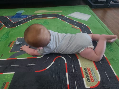 Customer's baby lying on their stomach on the green Kids Car Mat with a race track design.