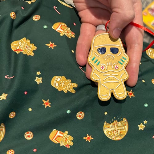 Reviewer holds a Star Wars gingerbread ornament, matching the festive pattern on the green performance hoodie.