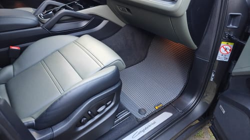 Recenzent pokazuje szary, dopasowany dywanik samochodowy na miejscu pasażera z przodu.