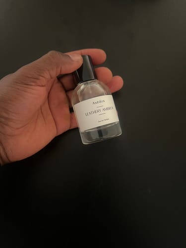 Customer's hand holding a clear bottle of Leathery Ambrox Eau de Parfum with a white label.