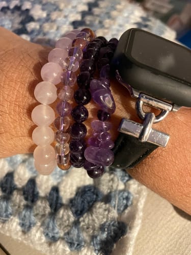 Client portant le bracelet de quartz rose au poignet, empilé avec d'autres bracelets violets et une montre.