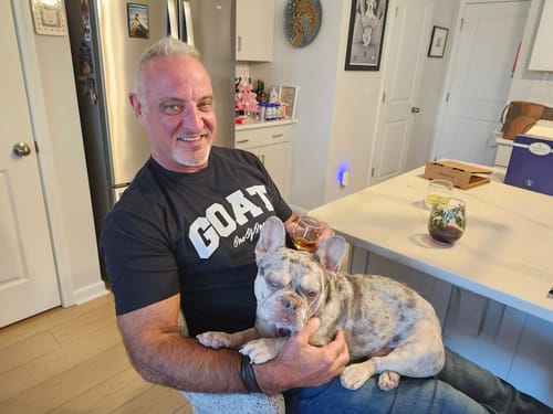 Customer smiling while wearing the black Goat Tee with a white logo and holding a dog.