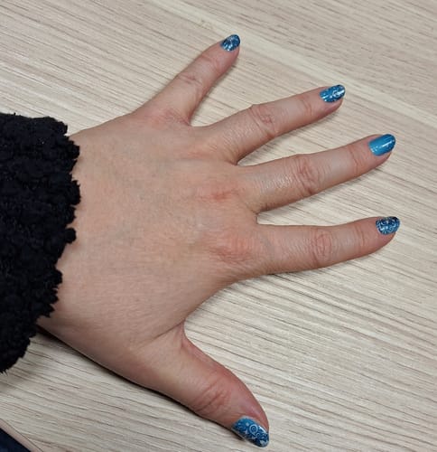 Hand einer Kundin, die eine Maniküre mit den eisblauen 'Fabulous Snow' Nagelfolien mit Schneeflockenmuster zeigt.
