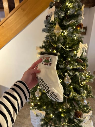 Customer holding a white Merry Beary sock with a bear graphic in front of a festive Christmas tree.