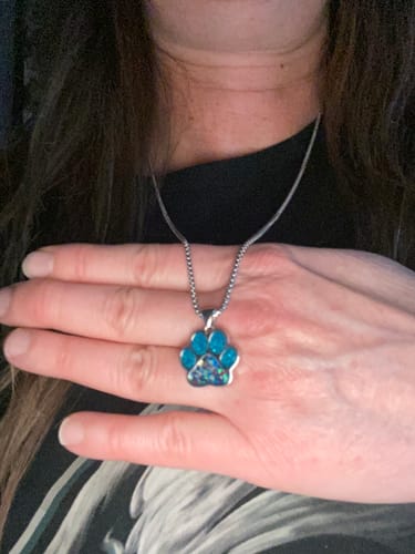 Customer holding a sparkly blue paw print pendant from a necklace against their chest.