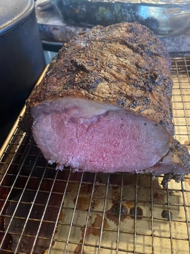 Customer's cooked Smoked Prime Rib on a wire rack, sliced to reveal a juicy pink center and dark crust.
