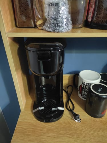 Cliente mostrando su cafetera Mainstays Single Serve negra nueva en una repisa de madera.