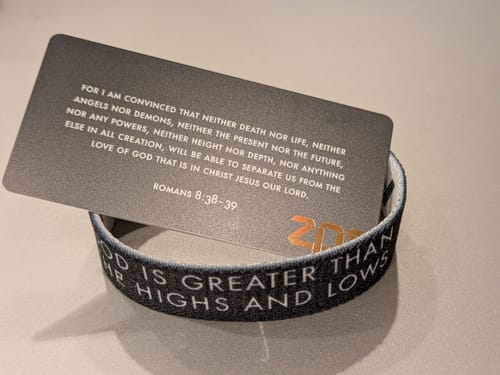 Customer's black God Is Greater bracelet showing the text 'GOD IS GREATER THAN THE HIGHS AND LOWS' with a verse card.