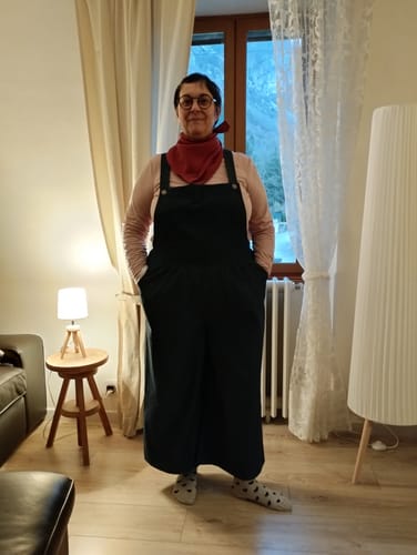 Une cliente porte la salopette ample Isaure en jean brut dans son salon.