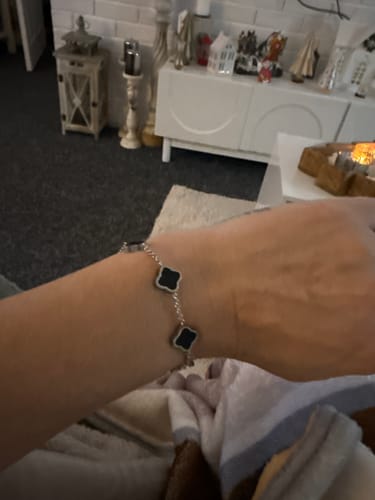 Customer's wrist wearing a silver-colored chain bracelet with black, four-leaf clover-shaped charms.
