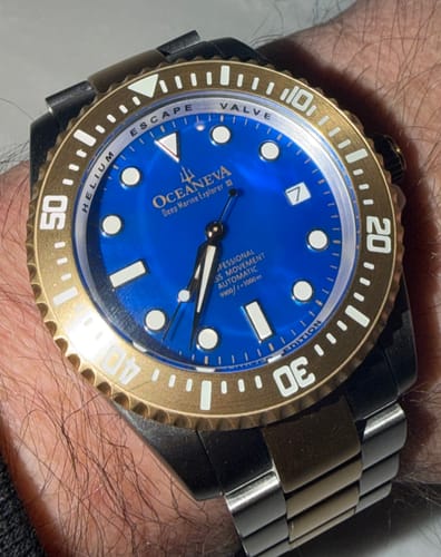 Close-up of a reviewer's Oceaneva watch on their wrist, showing the blue mother of pearl dial and yellow gold bezel in dim light.