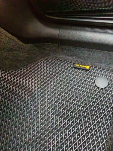 Klient pokazuje idealnie dopasowany czarny dywanik samochodowy z wzorem w romby we wnętrzu swojego auta.