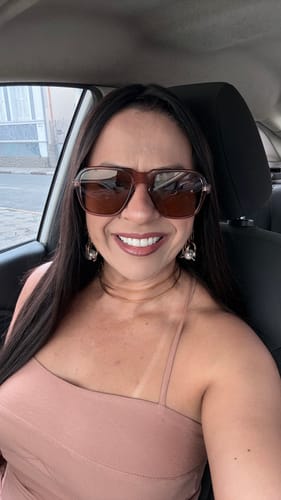 Cliente sorrindo dentro de um carro, usando os Óculos Messina de armação quadrada e lentes marrons.
