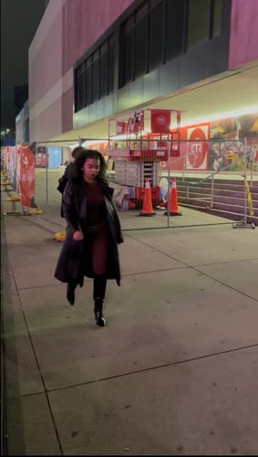 Partial view of a reviewer walking at night, wearing the dark NW Sculpt Crewneck Bodysuit under a long black coat.