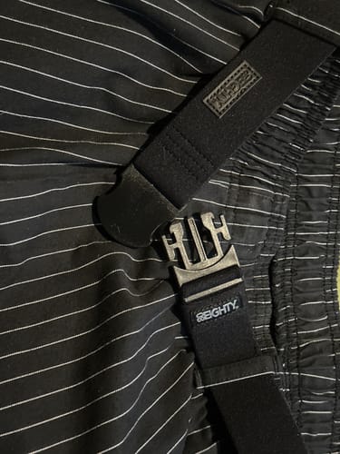 Customer's close-up of the black 80Eighty Resilient Belt, unbuckled and laying across striped pants.