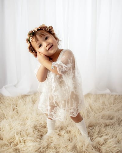 Customer's child posing in the lacy white Isabella Romper with a flower crown and socks.