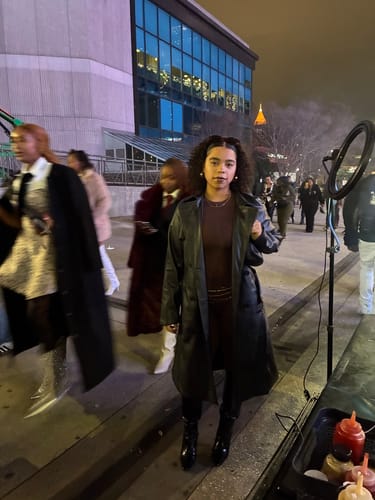 Customer standing outdoors at night wearing the dark, fitted NW Sculpt Crewneck Bodysuit under a black coat.