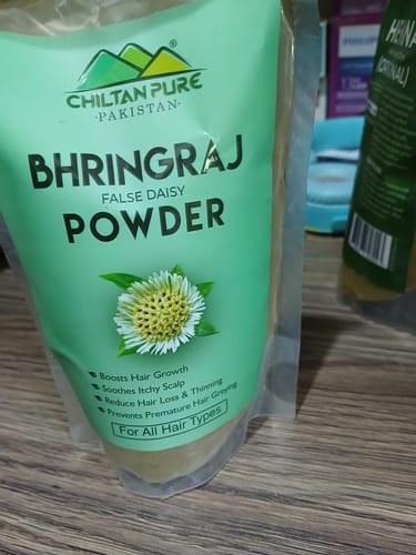 A customer's light green pouch of Chiltan Pure Bhringraj Powder sitting on a wooden table.