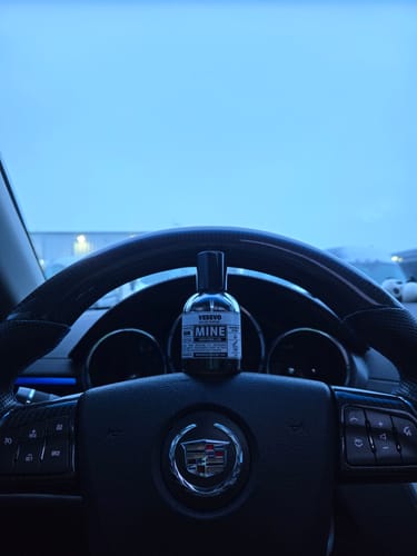 Recensore mostra il profumo VESEVO appoggiato sul volante di un'auto.