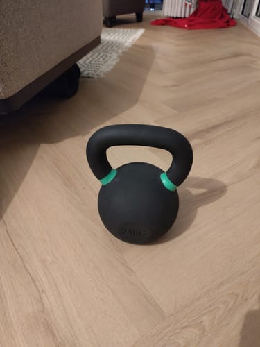 Reviewer's black 24kg Cast Iron Kettlebell with green handle bands on a wooden floor.