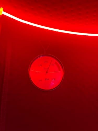 Close-up: A thermometer shows high heat inside a customer's red-lit Sauna Pod 2.0.
