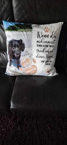 Das personalisierte Gedenkkissen eines Kunden mit dem Foto eines schwarzen Hundes liegt auf einem Ledersofa.