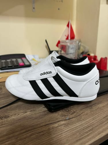 Customer's white and black adidas Tekwen Casual Shoes with a laceless strap, seen from the side on a desk.