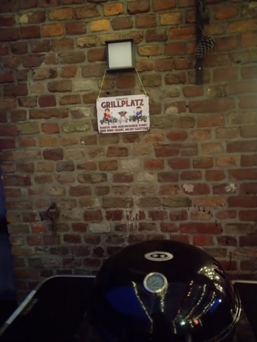 Ein Kunde zeigt das personalisierte Gartenschild, das an einer Backsteinwand über einem Grill hängt.