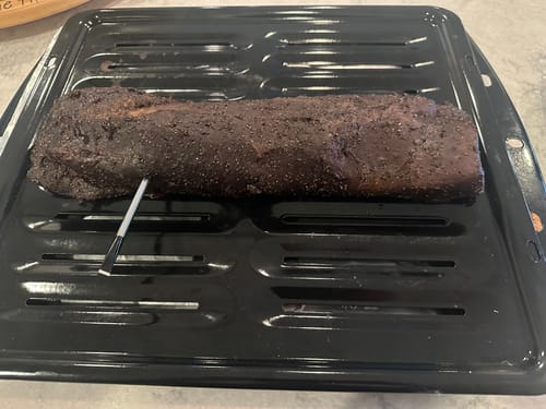 Customer's Pre-Cooked Smoked Beef Tenderloin resting on a black broiler pan with a meat thermometer inserted.