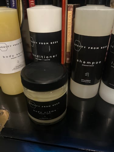 Customer's Body Crème in a small jar, displayed on a dark shelf alongside other products from the same line.
