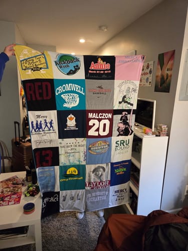 Customer holding up their completed, colorful Premium T Shirt Quilt in their room.