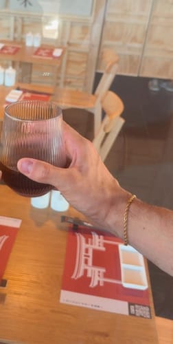 Cliente usando la Pulsera Rope Oro 3mm en la muñeca mientras sostiene una bebida en una mesa.