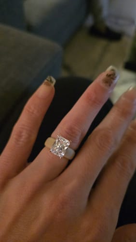 Customer's hand wearing the Silicone Ring with a large, emerald-cut CZ on a light-colored band.