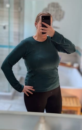 Reviewer taking a mirror selfie in a bathroom, showing the athletic fit of the green Hannah Long Sleeve Top.