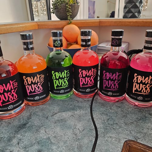 Customer's collection of colorful Sour Puss liqueur bottles lined up on a kitchen counter.