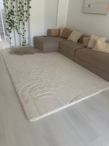 Customer's large, cream Mellow Mat with a carved pattern situated in front of a sofa in a living room.