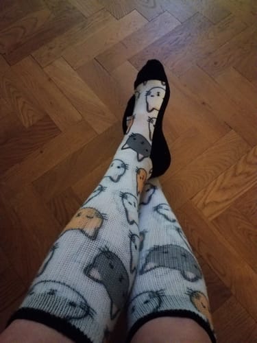 Kund som bär Diasocks Komfortstrumpor med ett gulligt kattmönster, med benen i kors på ett trägolv.