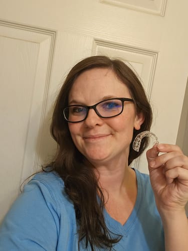 A smiling reviewer holds up a clear retainer.
