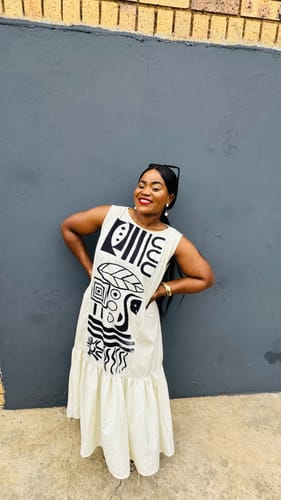 Customer smiling while posing in the white sleeveless long dress with a bold black graphic print on the front.